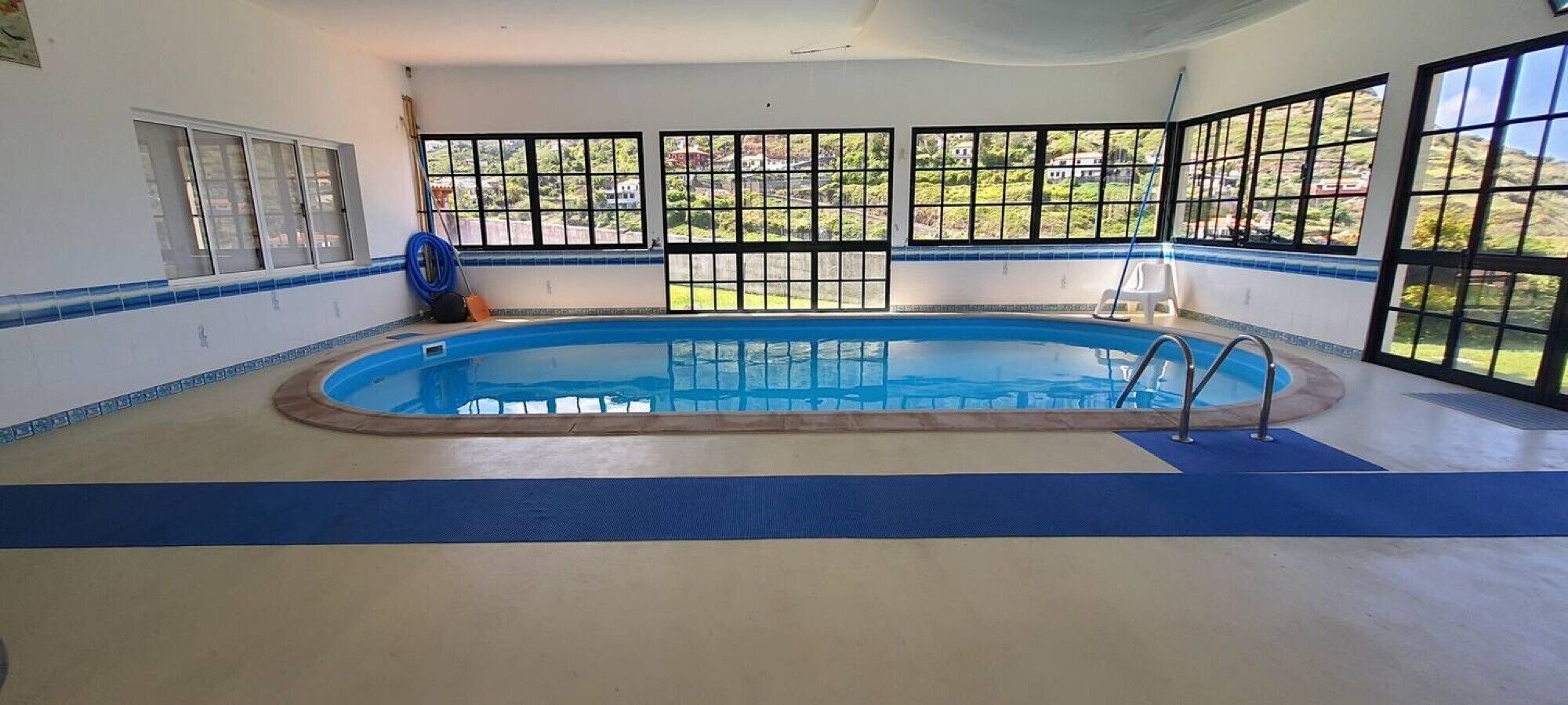 An indoor swimming pool with a view of a residential area through large windows.