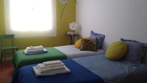 Una habitación con dos camas, una silla, una mesita y una ventana.