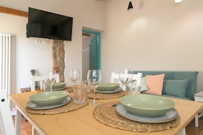 Une table à manger dressée avec des assiettes, des verres, et un téléviseur fixé sur un pilier en pierre.