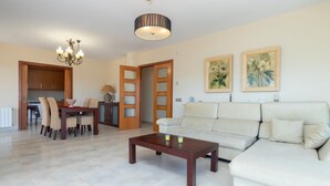 Un salon comprenant un canapé, une table à manger avec des chaises, une table basse, un lustre et deux tableaux encadrés accrochés au mur.