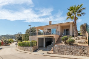 A two-story house with a balcony, a stone wall, and a palm tree.