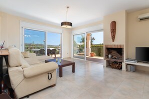 A spacious living room with a sofa, a coffee table, a fireplace, and large sliding glass doors. - Villa "Elodia" with Garden, Terrace, Pool & Wi-Fi (Calonge)