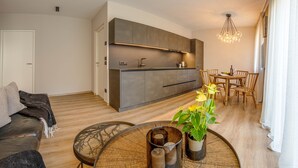 Ein modernes Wohnzimmer mit Sofa, Esstisch und Stühlen, einer Küchenzeile mit Schränken und einer Deckenleuchte.