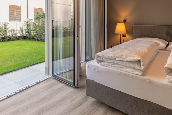 A bedroom with a bed, a nightstand, a lamp, and a sliding glass door leading to a balcony.