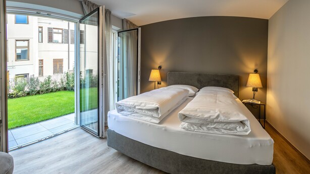Ein modernes Hotelzimmer mit einem gewölbten Bett, zwei Nachttischlampen und einer Glastür, die auf einen Balkon führt.