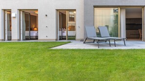 A modern building with a patio area, sliding glass doors leading to a bedroom, and a seating area with chairs.