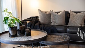 Ein Wohnzimmer mit einer Couch, zwei runden Tischen, einer Topfpflanze und Kerzen.