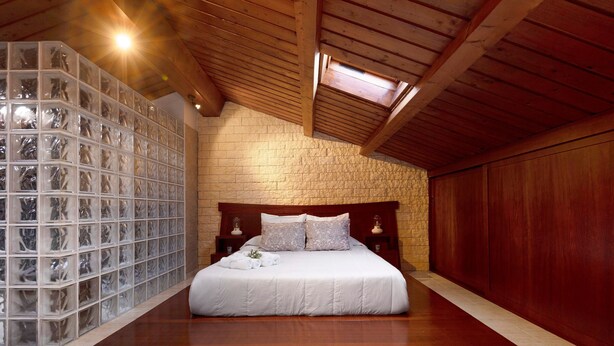 A bedroom with a wooden bed, a stone wall, and a skylight. - Holiday Home "Duplex India" with Wi-Fi (Tacoronte)