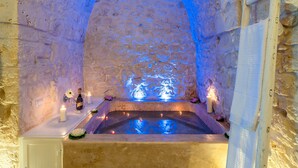 Een wellnessruimte met stenen muren, een bubbelbad, kaarsen en bloemen.