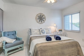 A bedroom with a bed, a chair, a nightstand, a lamp, and a window with blinds. - Ocean Breezes (St. Augustine)