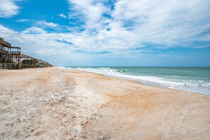 A beach with a wooden structure on the left, a sandy shore, and the ocean in the background. - Ocean Breezes (St. Augustine)