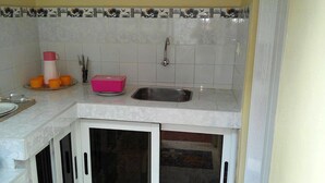 Una cocina con azulejos blancos, un lavamanos de acero inoxidable, un recipiente rosa y tazas naranjas sobre la encimera.