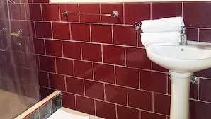 Un baño con lavamanos blanco, paredes de azulejos rojos, inodoro blanco y zona de ducha.