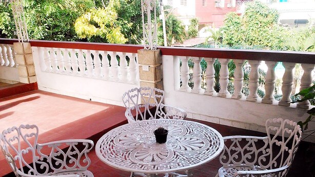 Un área de estar exterior con mobiliario de metal blanco, una mesa redonda y sillas, todo ello rodeado por una barandilla blanca.