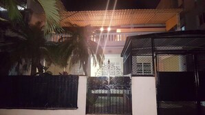 Zona residencial cerrada de noche, con una reja metálica, una palmera y un edificio con techo de lámina corrugada.