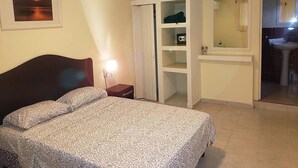 Un dormitorio con cama, mesita de noche, armario y baño visible a través de una puerta abierta.