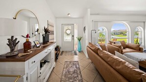 Ein modernes Wohnzimmer mit einer Couch, einem Couchtisch, einem Fernseher und einem großen Fenster mit Blick auf Grünflächen.