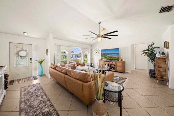 A spacious living room with a brown sofa, a coffee table, and a ceiling fan. - Tropical Oasis sleeps 13 with a heated pool. Free WiFi. Close to everything (Cape Coral)