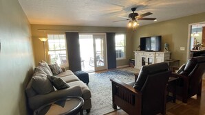 A living room with a sofa, armchairs, a coffee table, a TV, and a ceiling fan.