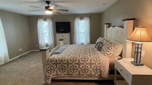 A bedroom with a bed, nightstand, lamp, ceiling fan, and a TV on a dresser.