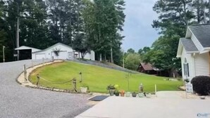 A residential street with houses, a grassy lawn, and a driveway.