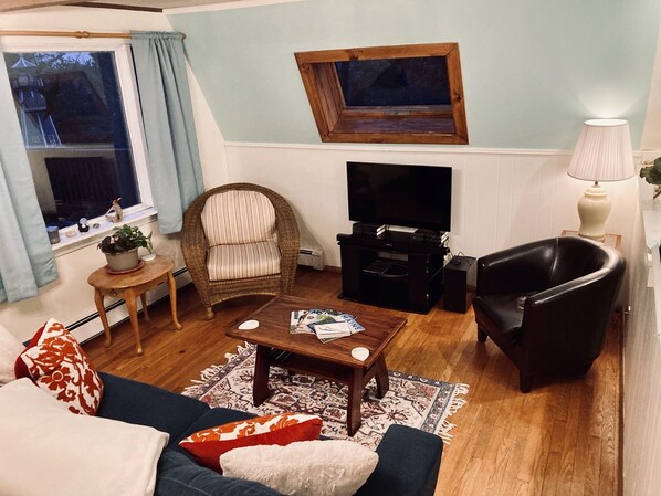 A living room with a sofa, armchair, coffee table, TV stand, and a window with curtains. - Sunny and Spacious A-Frame nestled in the fir trees. Mountain views! (Tremont)