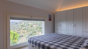 A bedroom with a large window, a bed with a checkered bedspread, and a wardrobe. - Italianway - Luxury Apartment in Modern Villa 2 (Imperia)