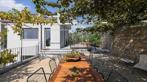Un patio exterior moderno con una mesa de madera, sillas y un muro de piedra.