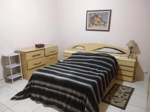 A bedroom with a bed, a dresser, a nightstand, and a lamp.