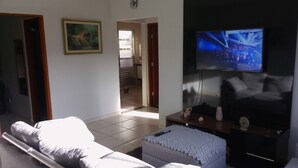 Una sala de estar con sofá, televisión montada en la pared, una mesita con objetos decorativos y una puerta que da a otra habitación.