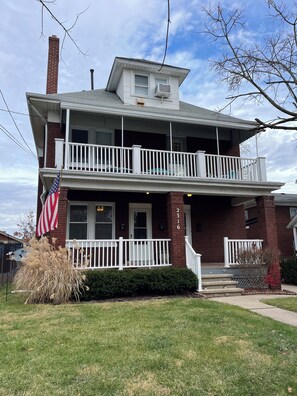 Uma casa de dois andares com varanda da frente, chaminé e uma bandeira americana.