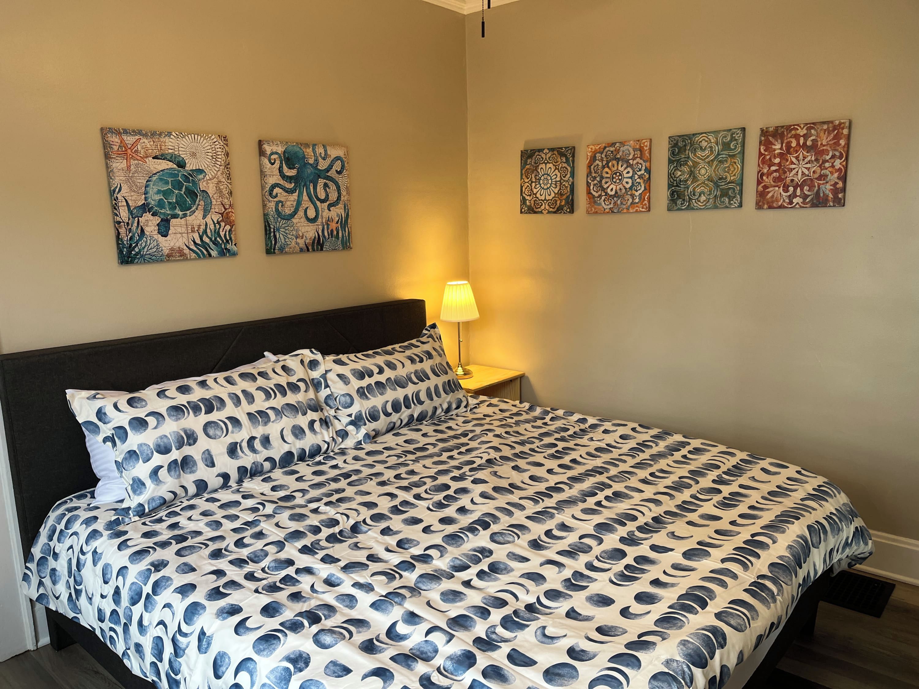 Une chambre à coucher comprenant un lit, une table de chevet et quatre œuvres d’art accrochées au mur.