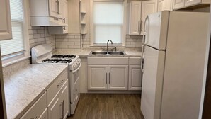 Une cuisine de taille réduite avec des meubles blancs, une cuisinière à gaz, un évier et un réfrigérateur.
