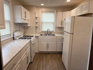 A compact kitchen with white cabinets, a gas stove, a sink, and a refrigerator.