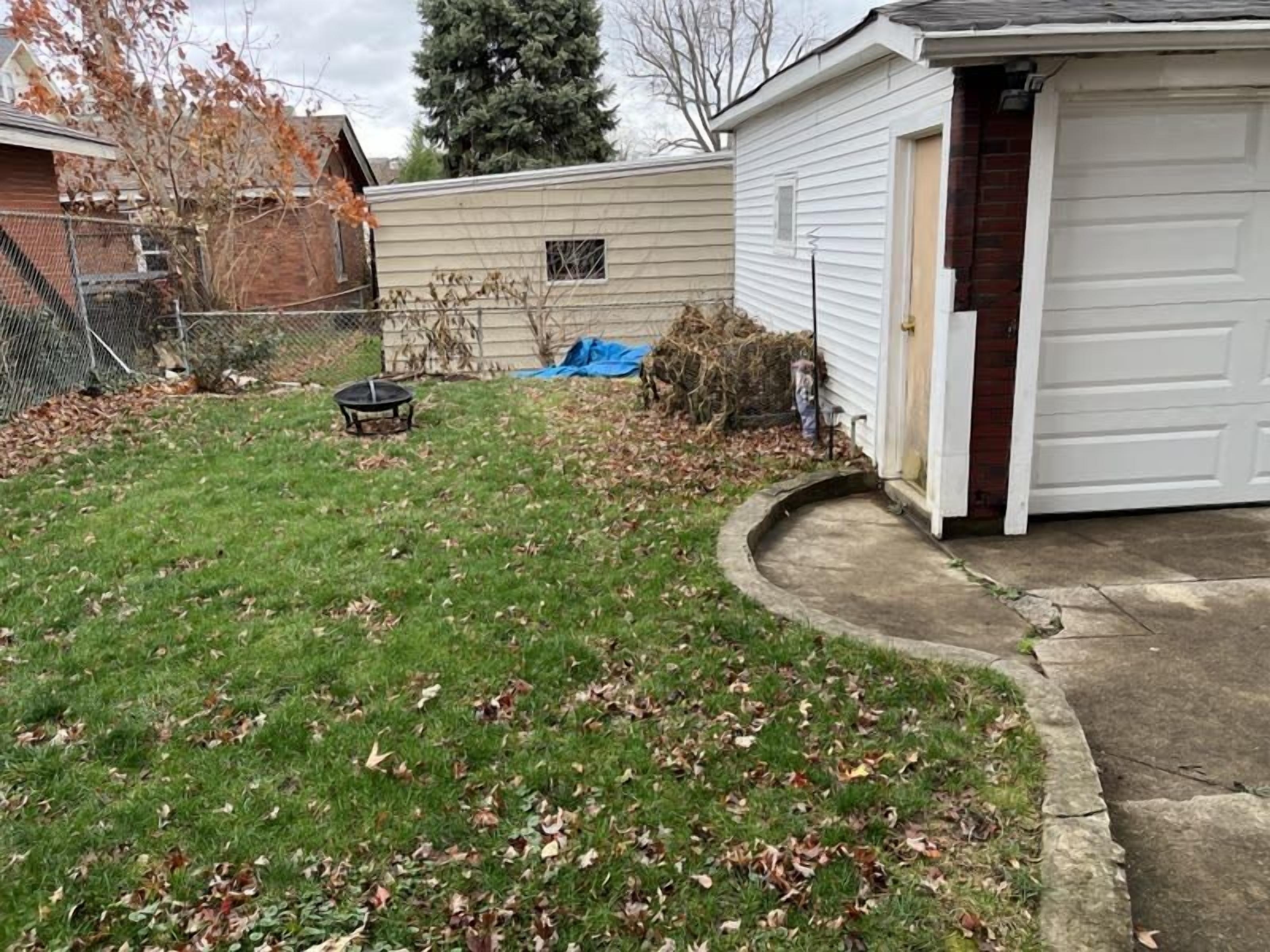 Eine Garage mit Wohnhausanschluss, eine weiße Tür, ein kleines Gartenhaus und ein Rasen mit herabgefallenen Blättern.