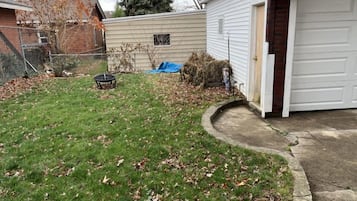 Eine Garage mit Wohnhausanschluss, eine weiße Tür, ein kleines Gartenhaus und ein Rasen mit herabgefallenen Blättern.