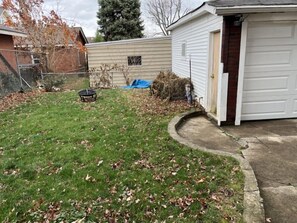 Eine Garage mit Wohnhausanschluss, eine weiße Tür, ein kleines Gartenhaus und ein Rasen mit herabgefallenen Blättern.