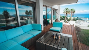 A balcony with a sofa, a table, and a view of the ocean.