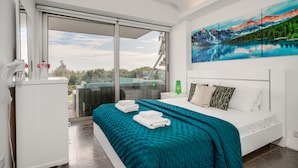 A modern hotel room with a large bed, a view of the outdoors, and a painting on the wall.