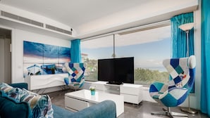 A modern living room with a large TV, a sofa, a coffee table, and a view of the outdoors.