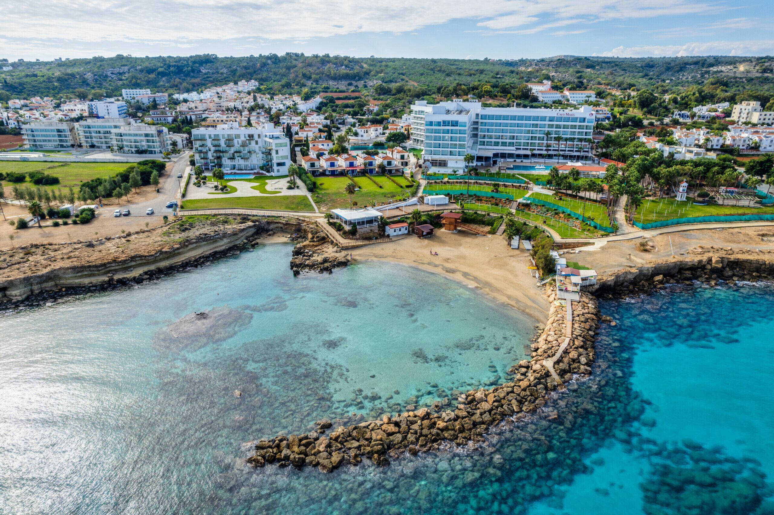 Un hotel frente al mar con varias construcciones, una playa y aguas azules cristalinas.