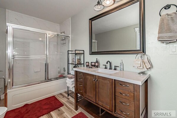 A bathroom with a glass shower enclosure, a large mirror, a vanity with a sink, and a towel rack.