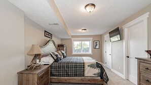 Ein Schlafzimmer mit Bett, Kommode, Lampe und Fenster.