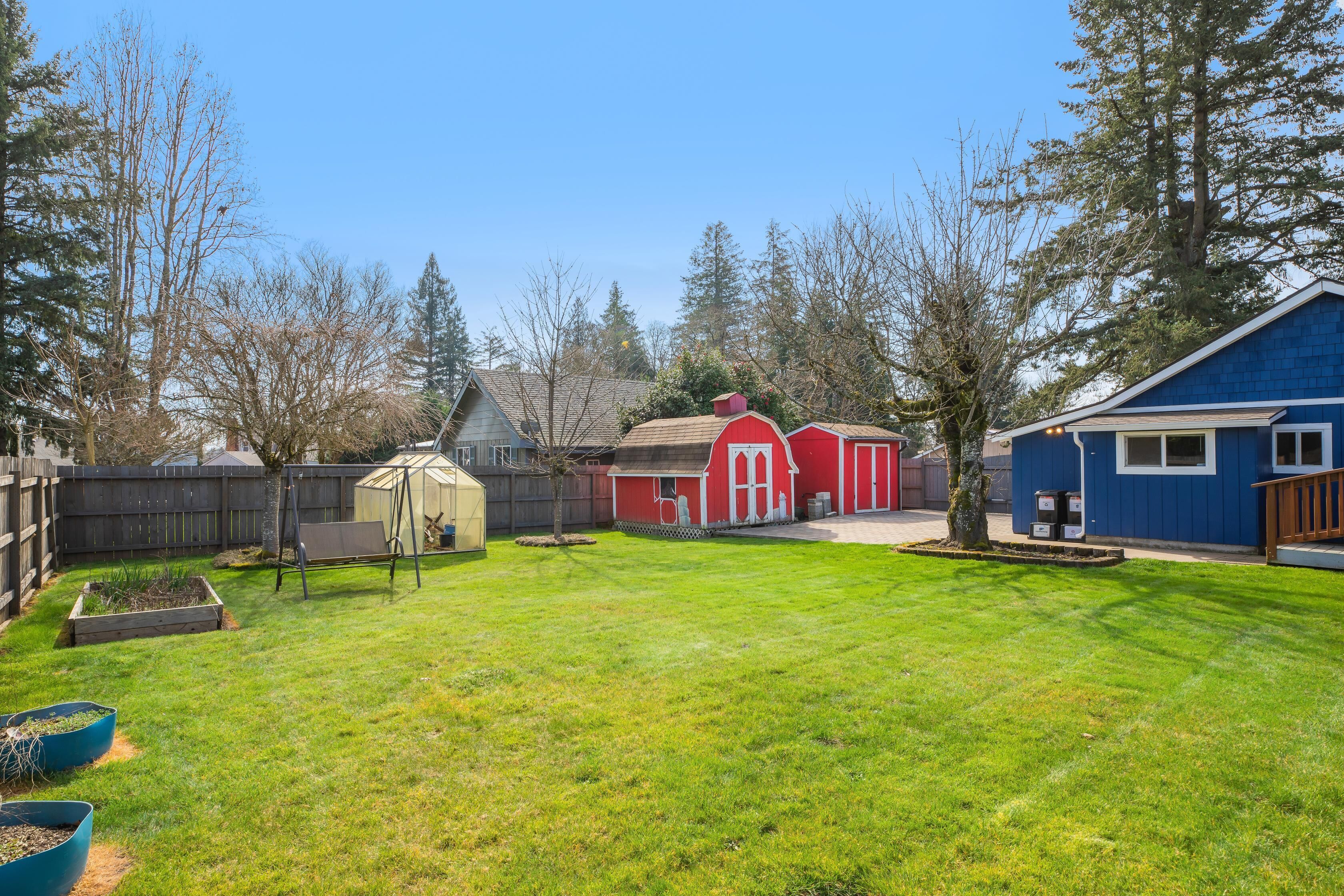 A backyard with a red barn, a blue house, and a wooden fence.
