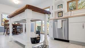 A kitchen with a central island, white cabinetry, a stainless steel refrigerator, and a dining area with wooden chairs and a table. - The Wayside: New in the Heart of Town (Dundee)