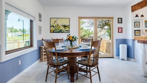 A dining area with a round table, six chairs, and a vase of flowers. A large window and sliding glass door provide views of the outdoors. - The Wayside: New in the Heart of Town (Dundee)