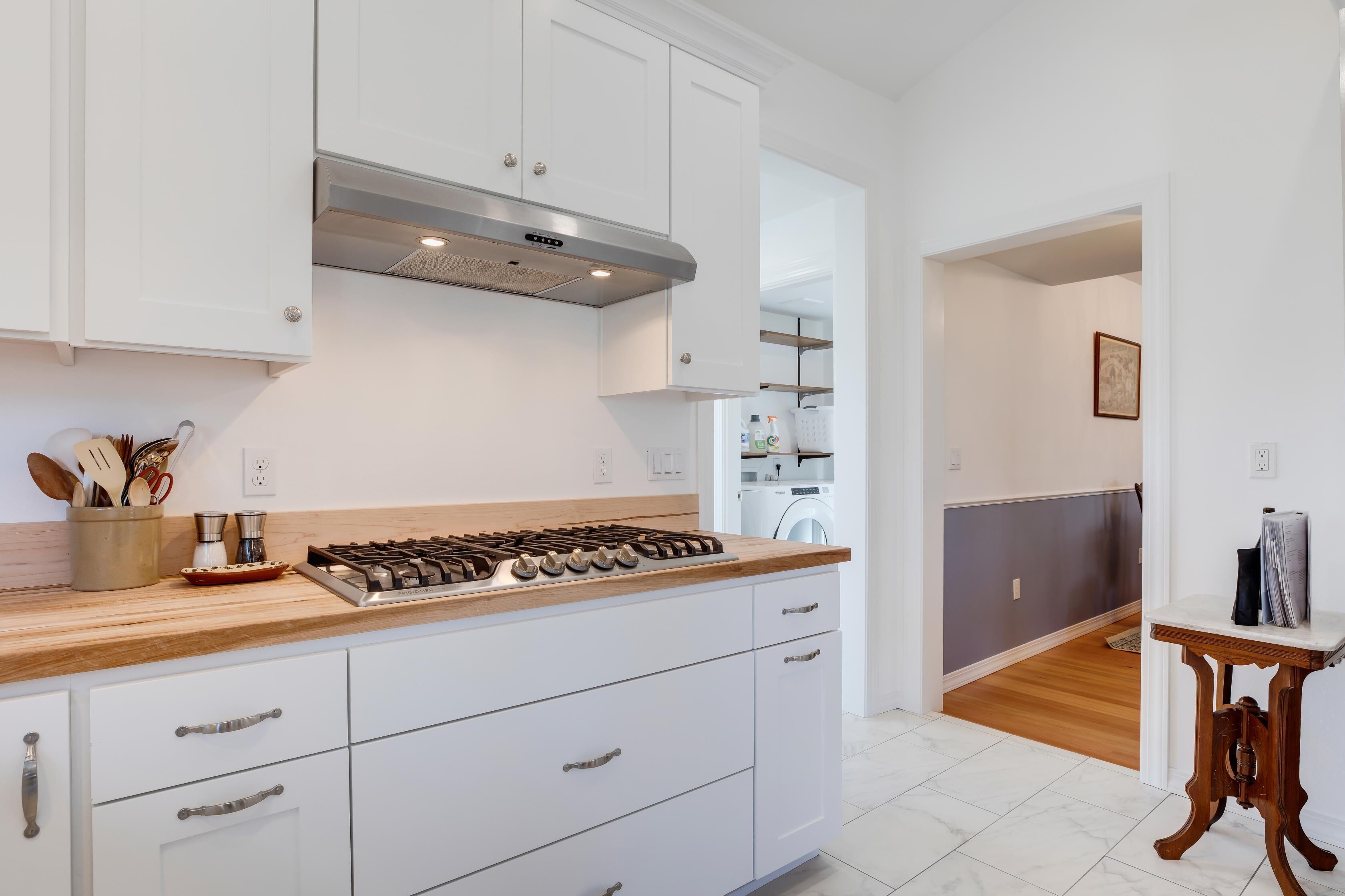 A modern kitchen with white cabinets, a wooden countertop, and a stainless steel range hood.