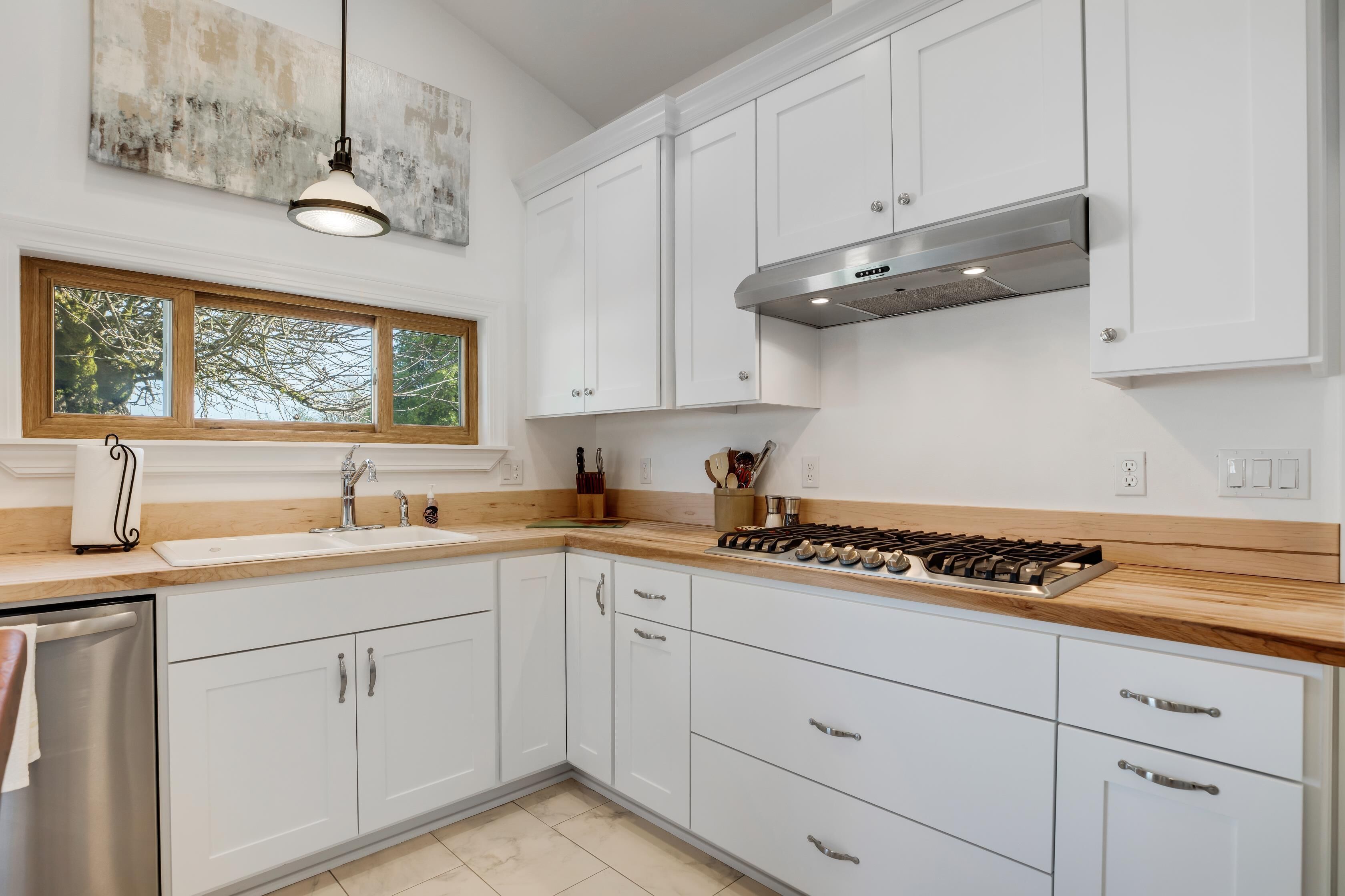 Una cocina moderna con armarios blancos, encimera de madera, estufa a gas y ventana con vista a árboles.