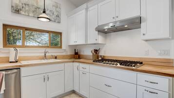 Una cocina moderna con armarios blancos, encimera de madera, estufa a gas y ventana con vista a árboles.