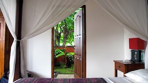 Una camera da letto con un letto, un comodino, una lampada rossa e vista su un giardino attraverso una porta aperta.